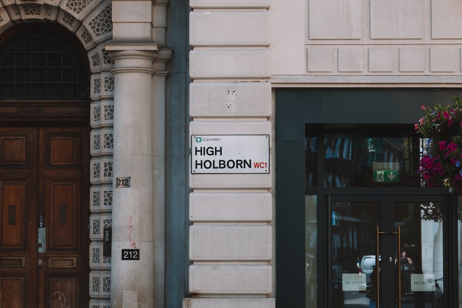 A close-up view of a building exterior showing a street sign reading 'High Holborn WC1' mounted on a white stone facade. To the left, a large wooden double door with decorative carvings and a modern i